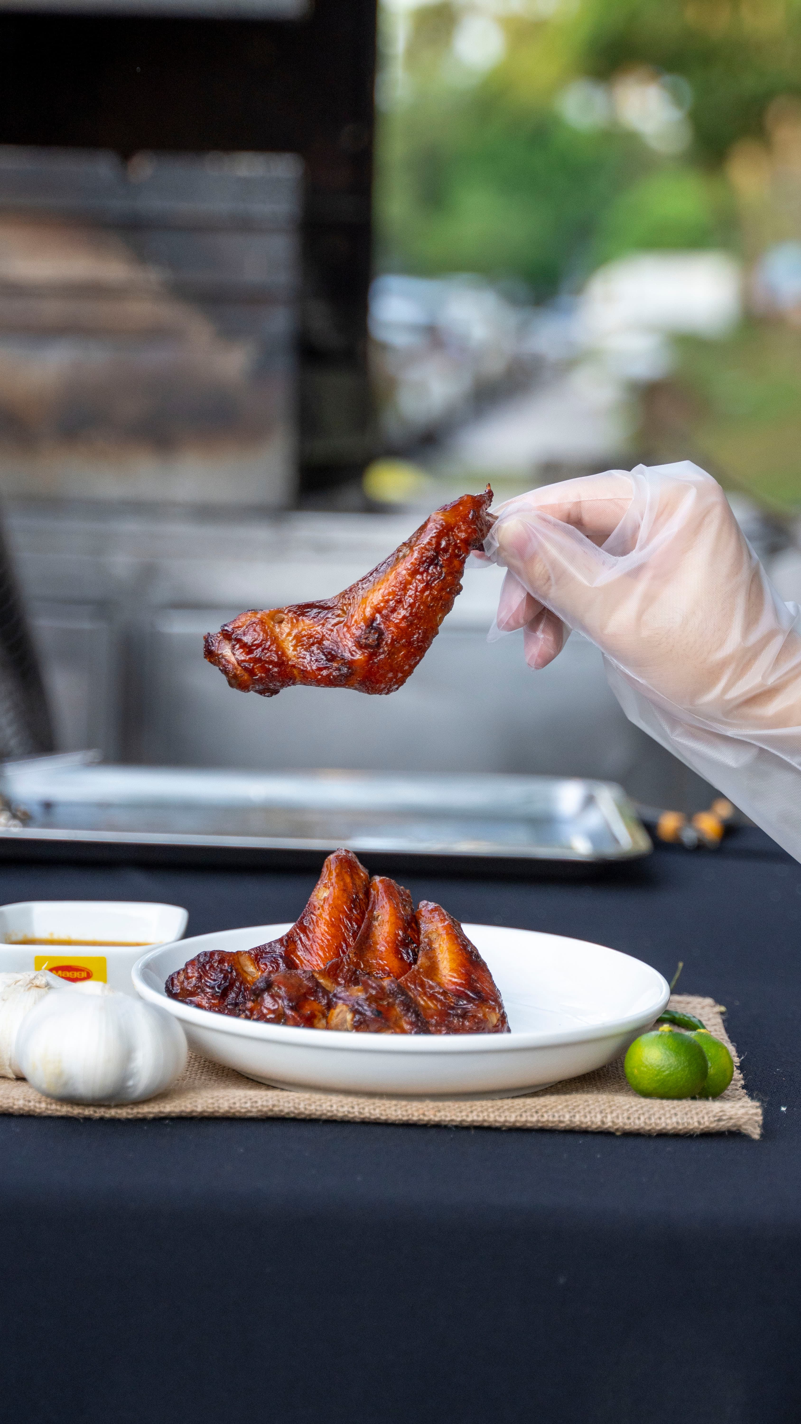 A gloved hand holding a grilled chicken wing above a plate of wings