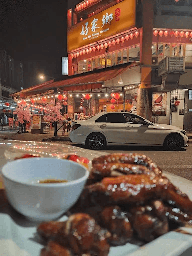 Chicken wings in the foreground with Hometown Hotpot’s illuminated storefront across the street at night
