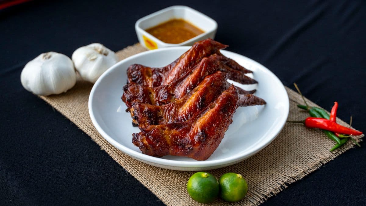 Grilled chicken wings served on a white plate with sauce, garlic, chillies and limes